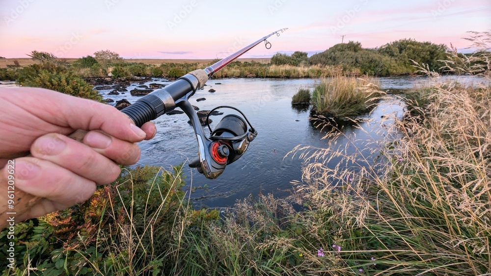 Hand holding fishing rod and reel, fishing at Corrib river at Galway, Ireland, spinning, angling, catch and release, sport and leisure, nature background