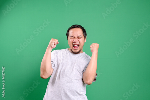 Portrait of satisfied Asian man celebrating success over green background