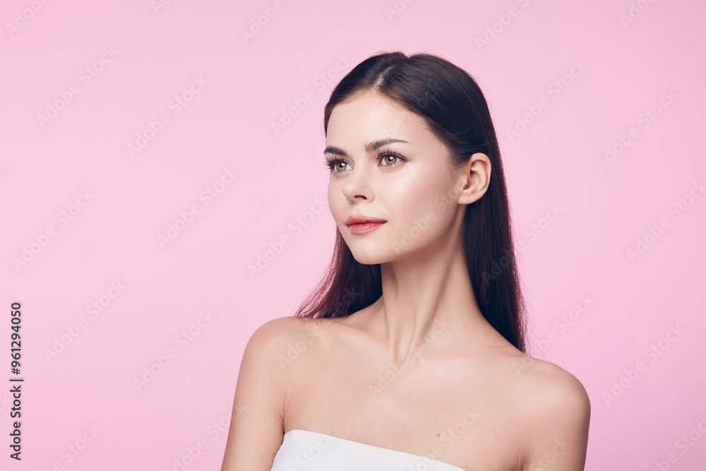 Fototapeta premium Beautiful young woman with long dark hair and white dress posing on a pink background with copy space