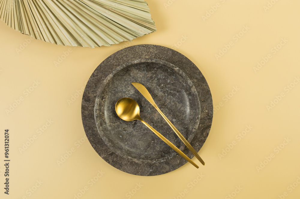 Top view of brown marble tray, plate and gold cutlery on yellow background. Dried palm leaf. Food presentation, dishes, stone tray. Copy space, flat lay. Top view of brown marble tray, plate and gold cutlery on yellow background. Dried palm leaf. Food presentation, dishes, stone tray. Copy space, flat lay.