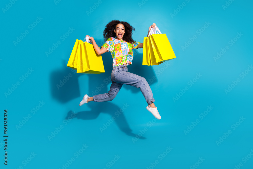 Full length photo of shiny attractive lady dressed flower print t-shirt jumping rising bargains empty space isolated blue color background Full length photo of shiny attractive lady dressed flower print t-shirt jumping rising bargains empty space isolated blue color background