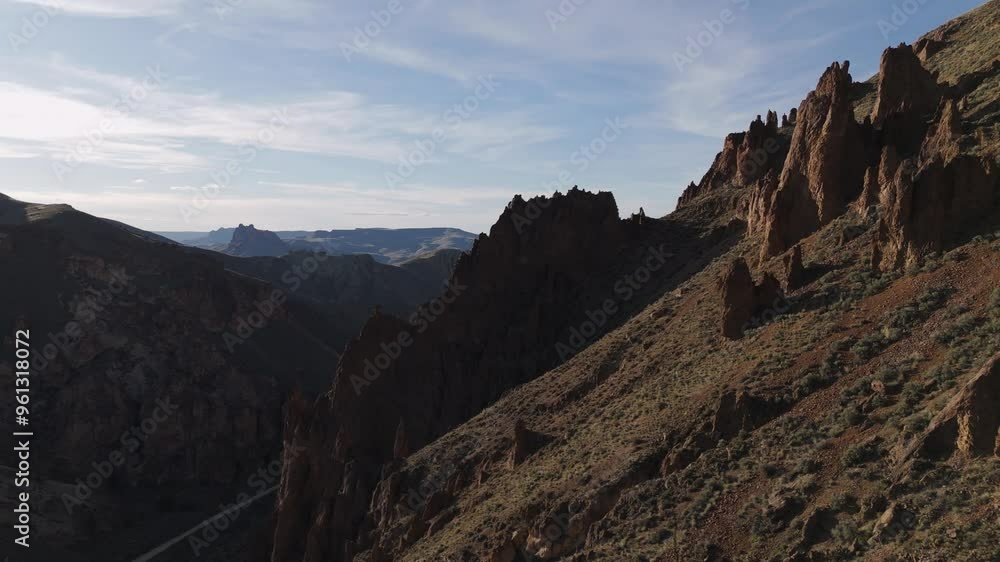 Drone tracking right to left along steep hillside at Leslie Gulch Oregon to reveal entire canyon and road at sunset Drone tracking right to left along steep hillside at Leslie Gulch Oregon to reveal entire canyon and road at sunset