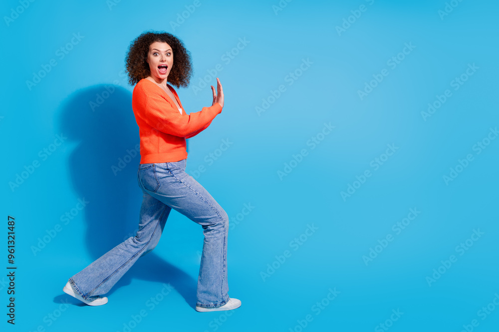 Photo portrait of wavy haired model woman wearing orange cardigan pushing heavy object isolated on blue color background Photo portrait of wavy haired model woman wearing orange cardigan pushing heavy object isolated on blue color background