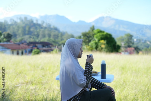 A Muslim woman is sitting relaxing enjoying tea in nature