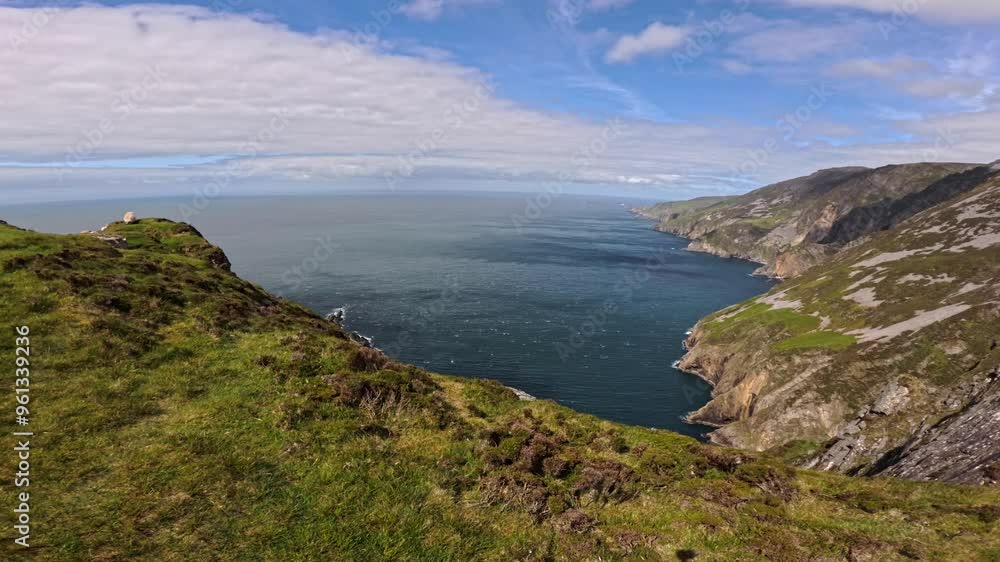 A static video of Slieve League cliffs in Ireland captures a lone sheep grazing on a green cliff. The view extends to a bay below, meeting the vast Atlantic Ocean A static video of Slieve League cliffs in Ireland captures a lone sheep grazing on a green cliff. The view extends to a bay below, meeting the vast Atlantic Ocean