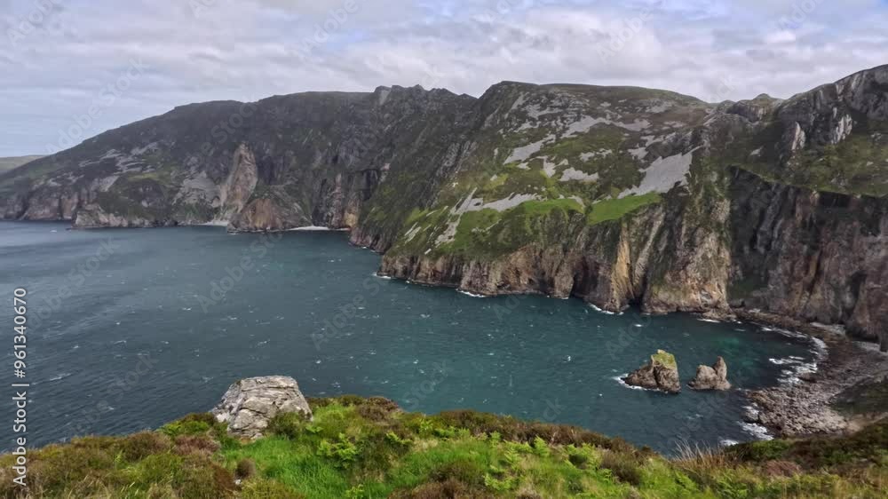 A wide panoramic video sweeps from right to left across the Slieve League cliffs in Ireland. The summer sun highlights the rugged terrain and deep blue waters of the Atlantic A wide panoramic video sweeps from right to left across the Slieve League cliffs in Ireland. The summer sun highlights the rugged terrain and deep blue waters of the Atlantic