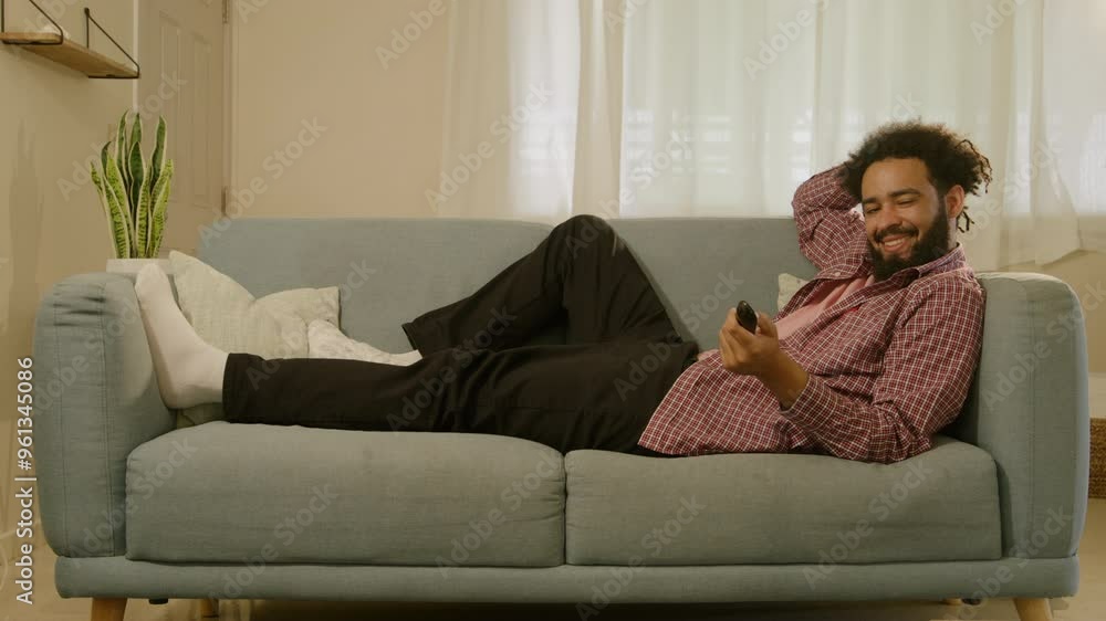 Young man comfortably lounges on a soft sofa, casually holding his cellphone while browsing the internet, embodying the essence of modern remote work, innovative ideas, and leisurely relaxation Young man comfortably lounges on a soft sofa, casually holding his cellphone while browsing the internet, embodying the essence of modern remote work, innovative ideas, and leisurely relaxation