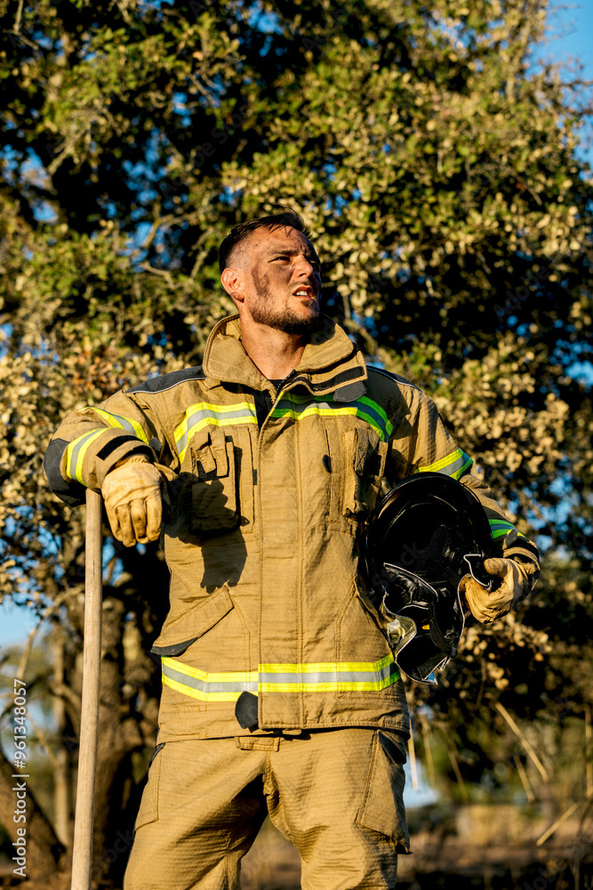 Firefighter holding helmet, standing in a sunlit forest Firefighter holding helmet, standing in a sunlit forest