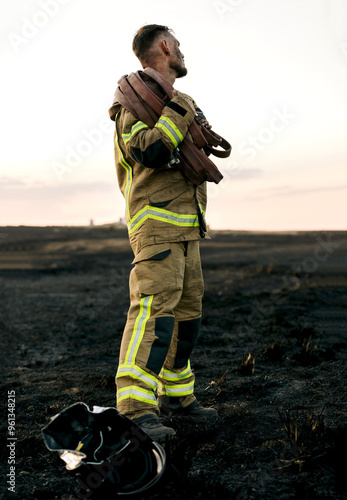 Firefighter holding hose in a burnt forest at dusk photo