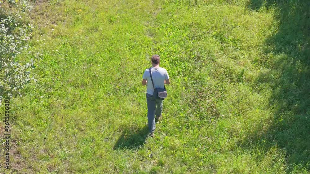 A man in linen pants and a light shirt strolls with his dog through fields and trees. A bag on his shoulder, he enjoys a sunny, clear day. A man in linen pants and a light shirt strolls with his dog through fields and trees. A bag on his shoulder, he enjoys a sunny, clear day.