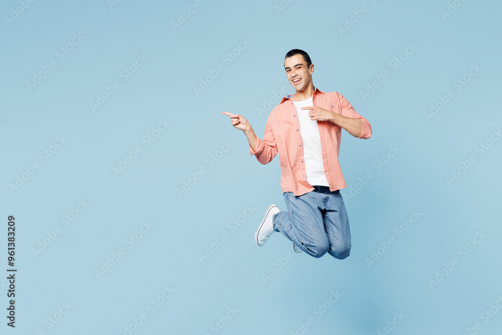 Obraz premium Full body young musician middle eastern man he wear pink shirt white t-shirt jump high point index finger aside on area isolated on plain pastel light blue cyan background studio. Lifestyle concept.