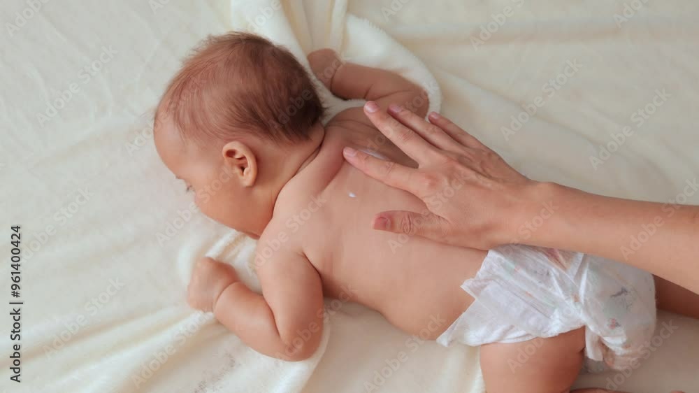 Infant little massage care. Kid's therapy. Health care and medicine. Anonymous mother or therapist making massage to her adorable newborn baby at home and applying moisturizing cream on his tiny back Infant little massage care. Kid's therapy. Health care and medicine. Anonymous mother or therapist making massage to her adorable newborn baby at home and applying moisturizing cream on his tiny back