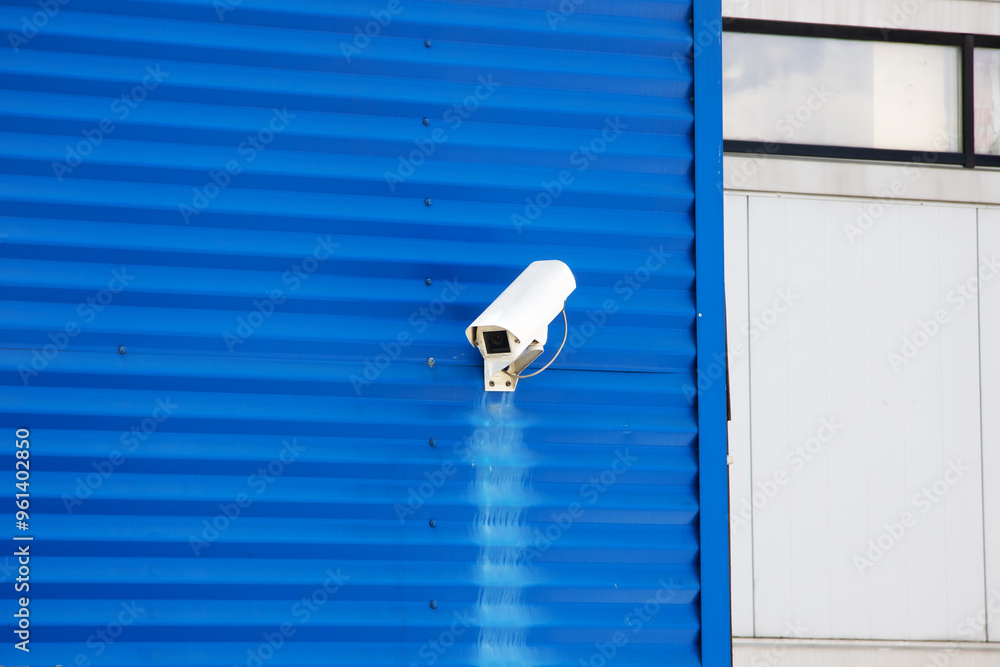 A security camera is mounted on the side of a blue colored building A security camera is mounted on the side of a blue colored building