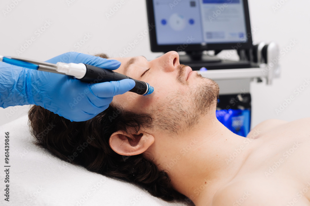 A man undergoes hydrofacial vacuum facial cleansing, rejuvenation, moisturizing facial procedure in a beauty clinic. Beauty and youth concept A man undergoes hydrofacial vacuum facial cleansing, rejuvenation, moisturizing facial procedure in a beauty clinic. Beauty and youth concept