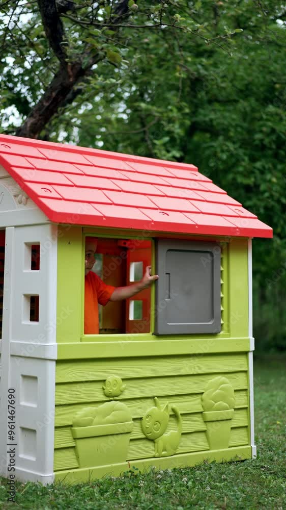 Charming boy opens the window of the play house from inside. Kid leaves the house and walks by the grass. Vertical video. Charming boy opens the window of the play house from inside. Kid leaves the house and walks by the grass. Vertical video.