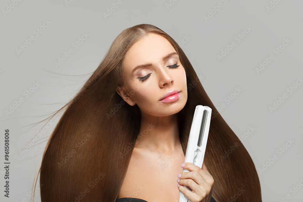 Indoor portrait of fashion model woman using hair straighteners iron on white background. Harstyle, hair care, beauty salon and treatment concept Indoor portrait of fashion model woman using hair straighteners iron on white background. Harstyle, hair care, beauty salon and treatment concept
