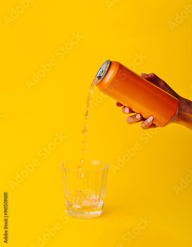 фотографія Woman pouring orange drink from can into glass on yellow background