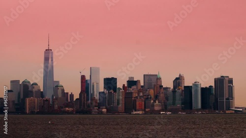 Fixed shot of Manhattan's skyline during pink sunrise, showcasing high-rise skyscrapers and calm river in foreground. Soft lighting highlights the city's iconic architecture. Manhattan, New York, USA
