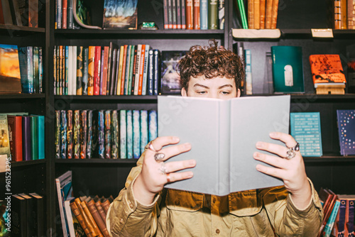Young man reading book near shelf in bookstore