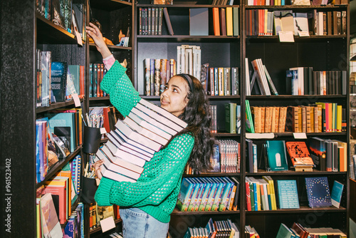Girl with heap of books reaching at shelf while standing in bookstore