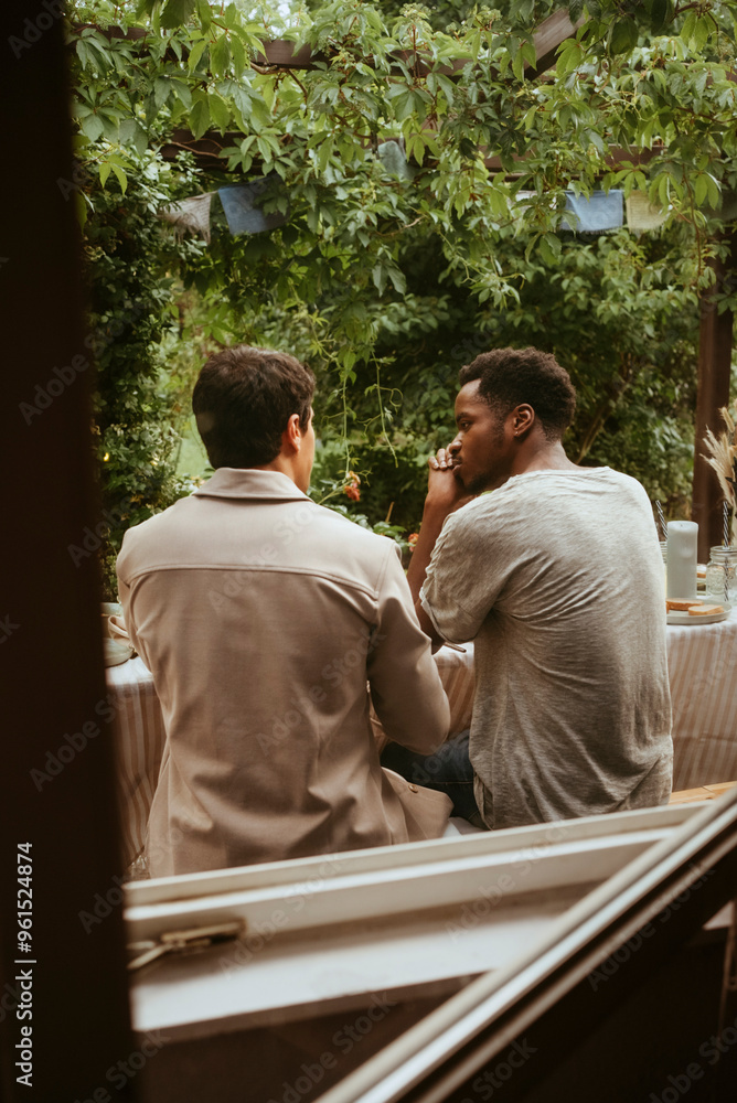 Rear view of young male friends talking with each other seen through window Rear view of young male friends talking with each other seen through window