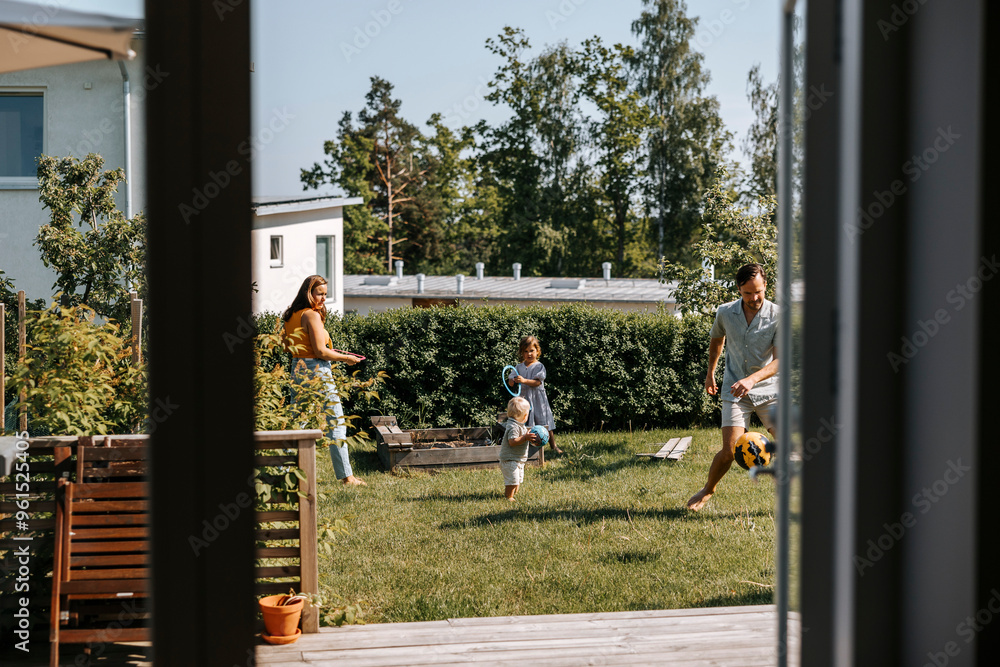 Father and mother playing with children in back yard seen through doorway Father and mother playing with children in back yard seen through doorway