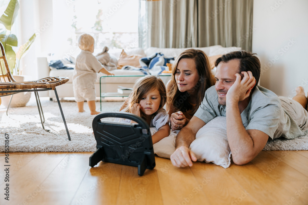 Father and mother watching tablet PC while lying down with daughter on floor at home Father and mother watching tablet PC while lying down with daughter on floor at home
