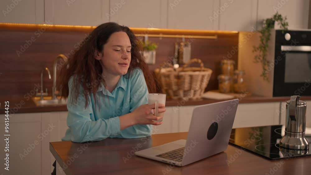 A woman sips her coffee and smiles at her laptop, surrounded by a well-decorated kitchen in a warm, inviting atmosphere. A woman sips her coffee and smiles at her laptop, surrounded by a well-decorated kitchen in a warm, inviting atmosphere.