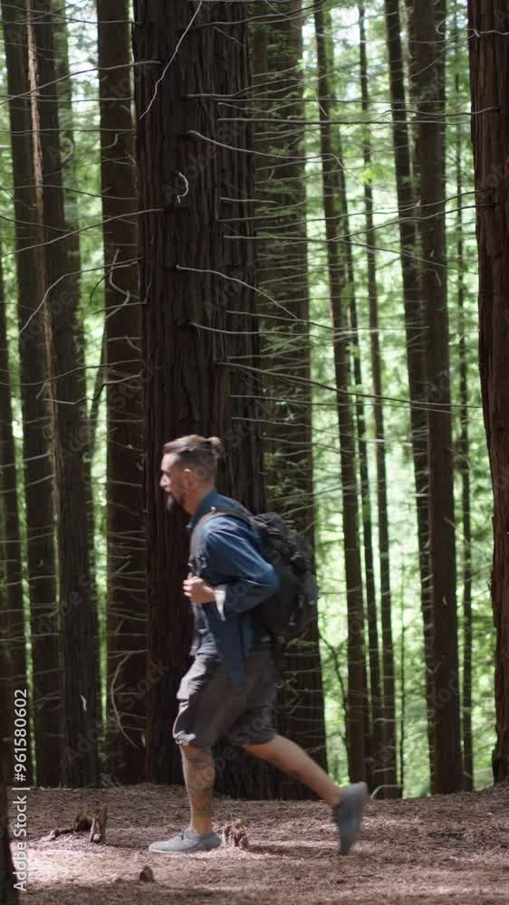 Vertical. Young Caucasian man strolling in forest among ancient trees enjoying time in nature. Sporty male adult person hiking in mountains on sunny spring day. People connecting with nature outdoors Vertical. Young Caucasian man strolling in forest among ancient trees enjoying time in nature. Sporty male adult person hiking in mountains on sunny spring day. People connecting with nature outdoors