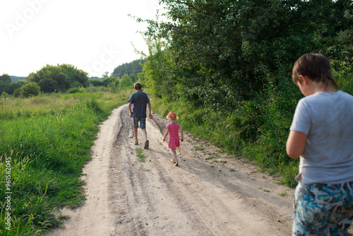 Children walking down a dirt road in a lush green landscape during the golden hour of late afternoon