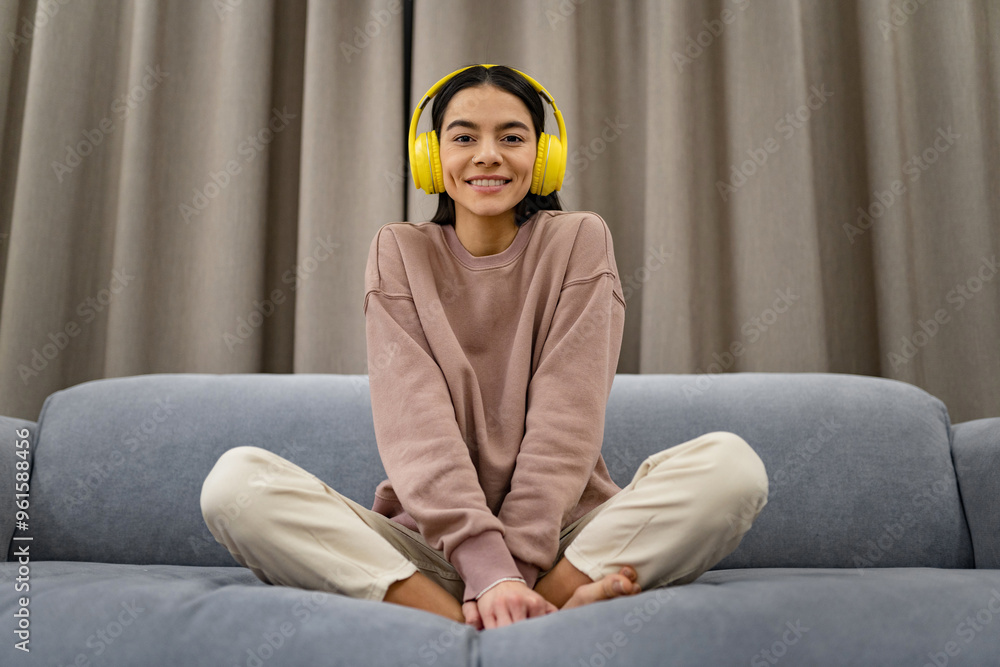 young woman at home in casual outfit sitting on sofa happy in yellow headphones listening to music young woman at home in casual outfit sitting on sofa happy in yellow headphones listening to music