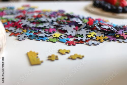 Colorful jigsaw puzzle pieces, cup of tea or coffee, eyeglasses and fresh berries for snacking. Hygge at home. Selective focus.