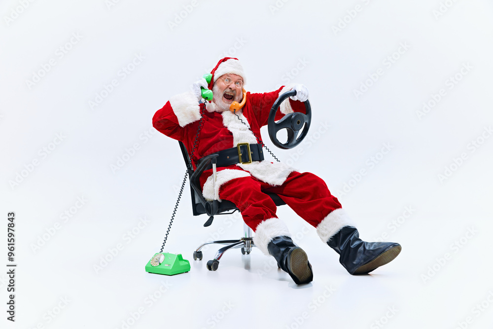Santa chats on two phones, green and orange, while gripping steering wheel with enthusiasm, reclining in his office chair with joyful look. Concept of winter holidays, Holly Jolly mood, celebration. Santa chats on two phones, green and orange, while gripping steering wheel with enthusiasm, reclining in his office chair with joyful look. Concept of winter holidays, Holly Jolly mood, celebration.