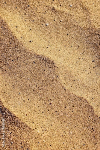 Golden sand texture with small pebbles, creating wavy patterns under sunlight.