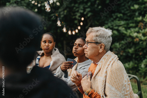 Senior man making face with family members and playing cards at garden party photo