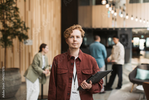 Portrait of young male delegate holding folder while standing at convention center