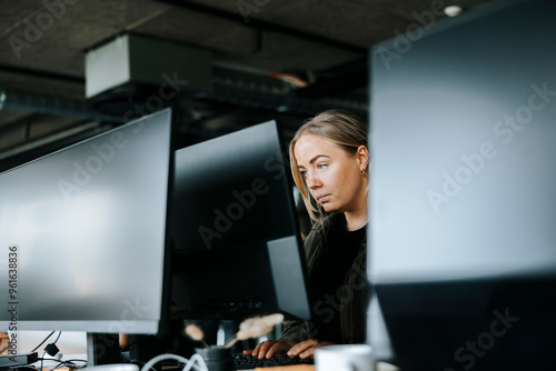 Focused female programmer doing coding on computer while sitting at desk in office