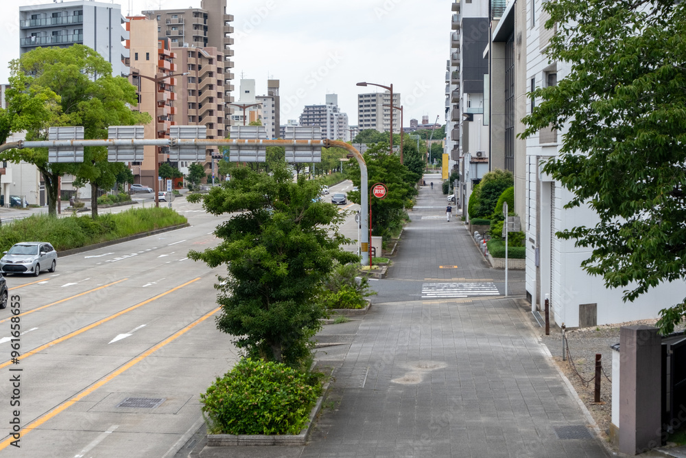 Elevated Japanese city view of Nagoya. A wide, multi-lane road with a pedestrian sidewalk, lined with urban buildings including apartment buildings and commercial establishments. Nagoya, Japan Elevated Japanese city view of Nagoya. A wide, multi-lane road with a pedestrian sidewalk, lined with urban buildings including apartment buildings and commercial establishments. Nagoya, Japan