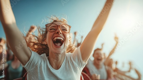 An exhilarating moment captured as a woman enjoys a thrilling roller coaster ride with outstretched arms and a background of other excited riders and clear blue sky. photo