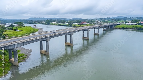 Aerial view of a concrete bridge spanning a calm river on a cloudy day