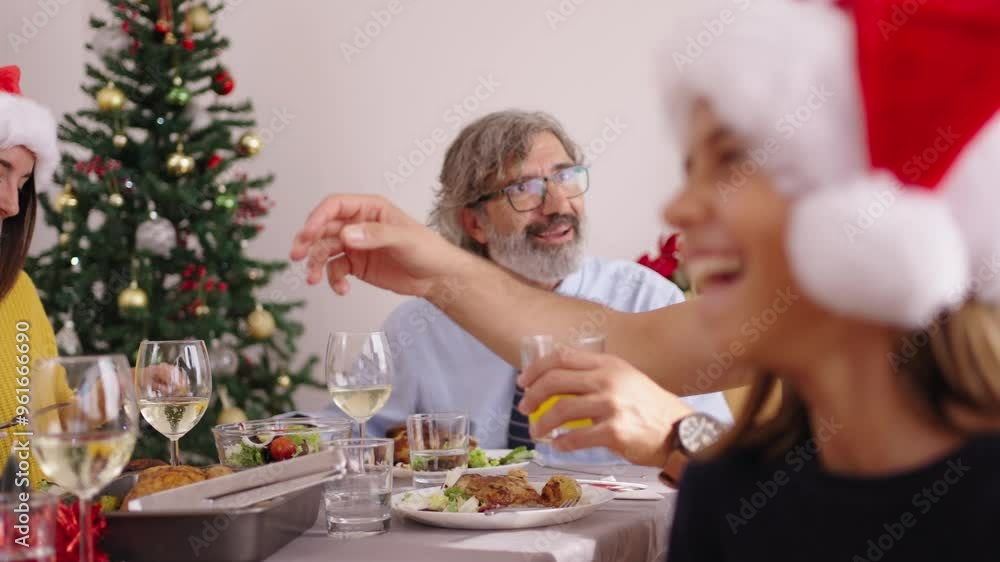 Focused and unfocused close-up side view of Caucasian girl laughing happy at family gathering at home wearing Christmas hat. Diverse people sitting cheerful at table celebrating festive meal indoors Focused and unfocused close-up side view of Caucasian girl laughing happy at family gathering at home wearing Christmas hat. Diverse people sitting cheerful at table celebrating festive meal indoors