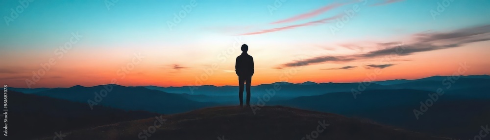© taweesak - A silhouette of a person standing on a hilltop at dusk, their shadow blending into the twilight sky The mood is contemplative and serene