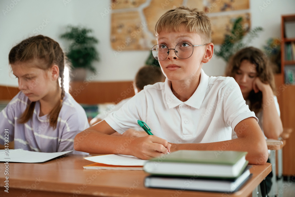 Sitting by the desks. Pupils, kids in the classroom together Sitting by the desks. Pupils, kids in the classroom together