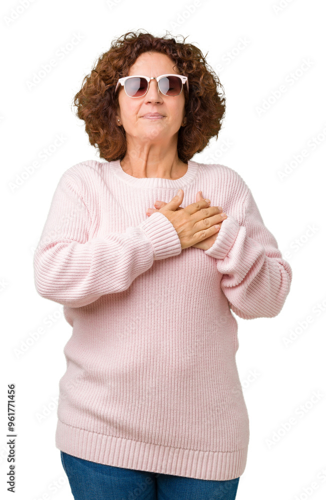 Beautiful middle ager senior woman wearing pink sweater and sunglasses over isolated background smiling with hands on chest with closed eyes and grateful gesture on face. Health concept. Beautiful middle ager senior woman wearing pink sweater and sunglasses over isolated background smiling with hands on chest with closed eyes and grateful gesture on face. Health concept.