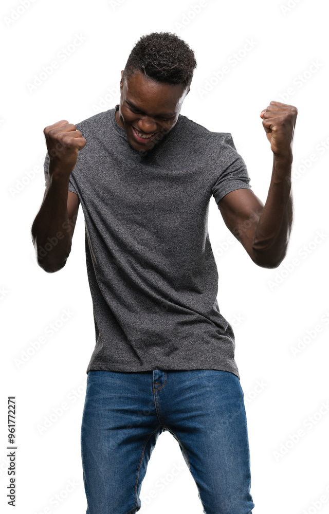 Young african american man wearing grey t-shirt very happy and excited doing winner gesture with arms raised, smiling and screaming for success. Celebration concept. Young african american man wearing grey t-shirt very happy and excited doing winner gesture with arms raised, smiling and screaming for success. Celebration concept.