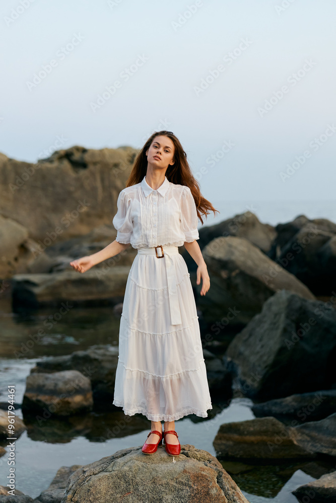 Woman in white dress embracing the ocean breeze on rocky shoreline Woman in white dress embracing the ocean breeze on rocky shoreline