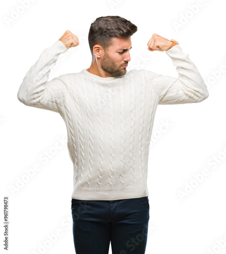 Young handsome man wearing winter sweater over isolated background showing arms muscles smiling proud. Fitness concept.