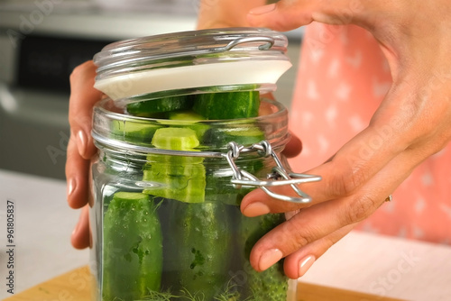 Woman putting cucumbers in glass jar to cook pickles closing lid on kitchen at home, hands close-up. Cuisine, culinary, prepare cook dish, domestic food, recipe, fresh organic ingredients concept.