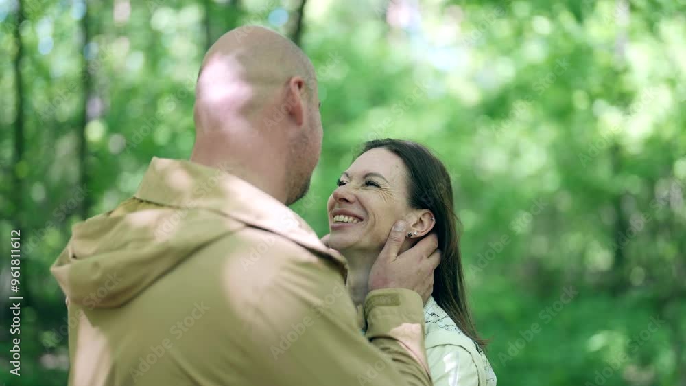 A couple in light jackets walk hand in hand through the forest. A woman holds a small bouquet in her hands, and a man with a slight smile looks into the distance, enjoying nature. A couple in light jackets walk hand in hand through the forest. A woman holds a small bouquet in her hands, and a man with a slight smile looks into the distance, enjoying nature.