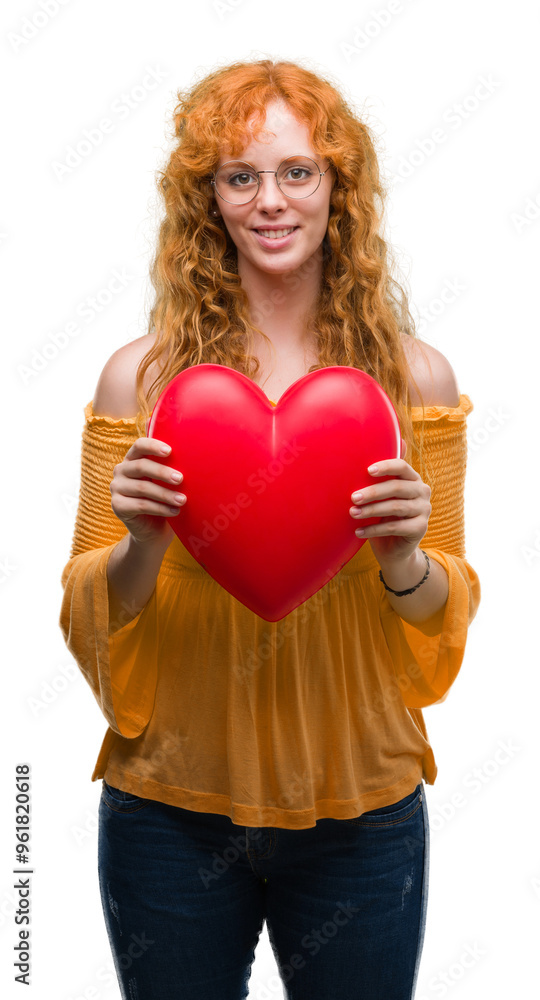 Young redhead woman in love holding red heart with a happy face standing and smiling with a confident smile showing teeth Young redhead woman in love holding red heart with a happy face standing and smiling with a confident smile showing teeth